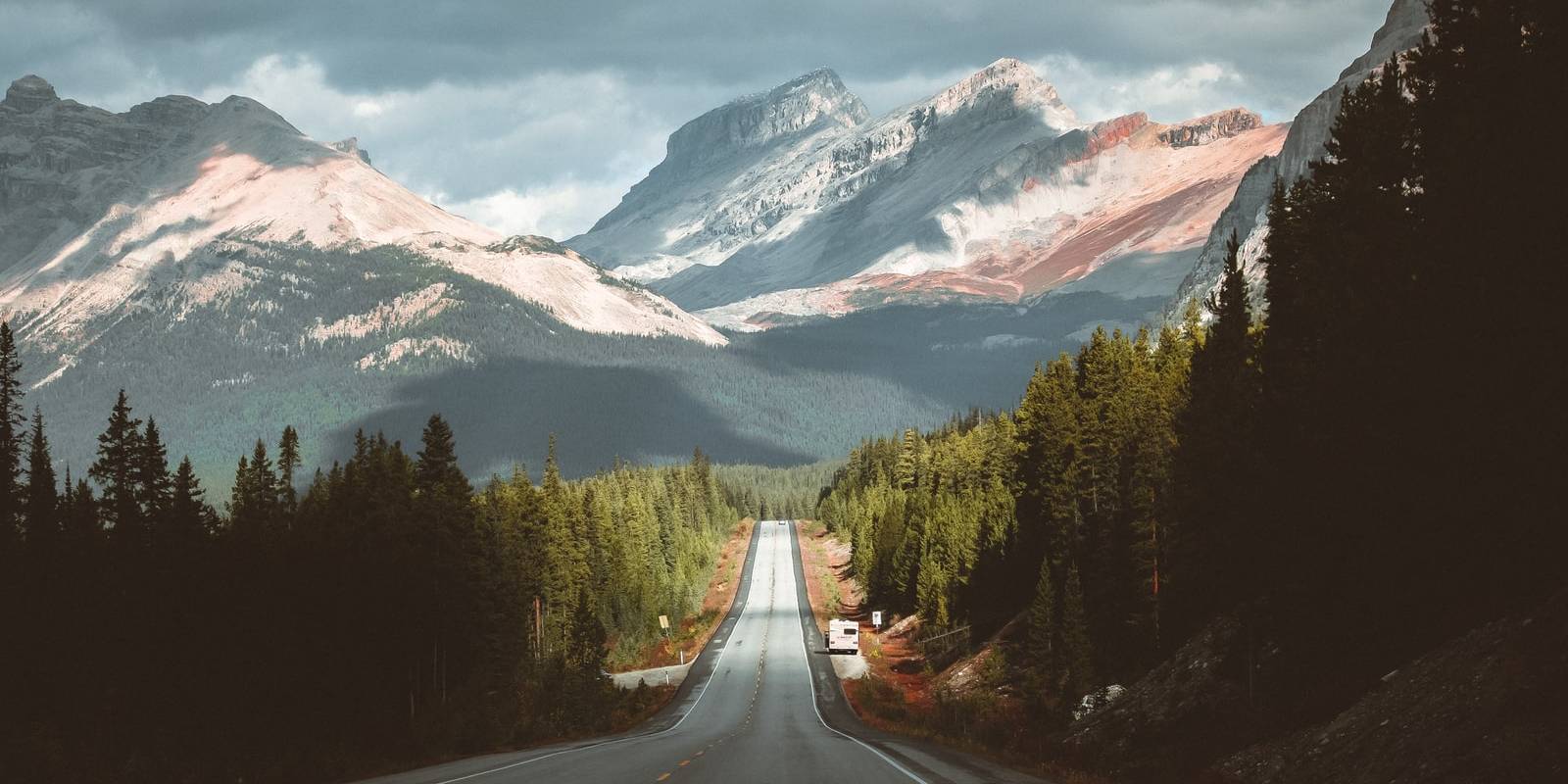 gray concrete road between green trees and mountains during daytime