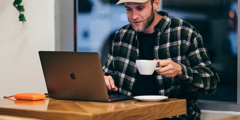 man sitting while having coffee and using laptop